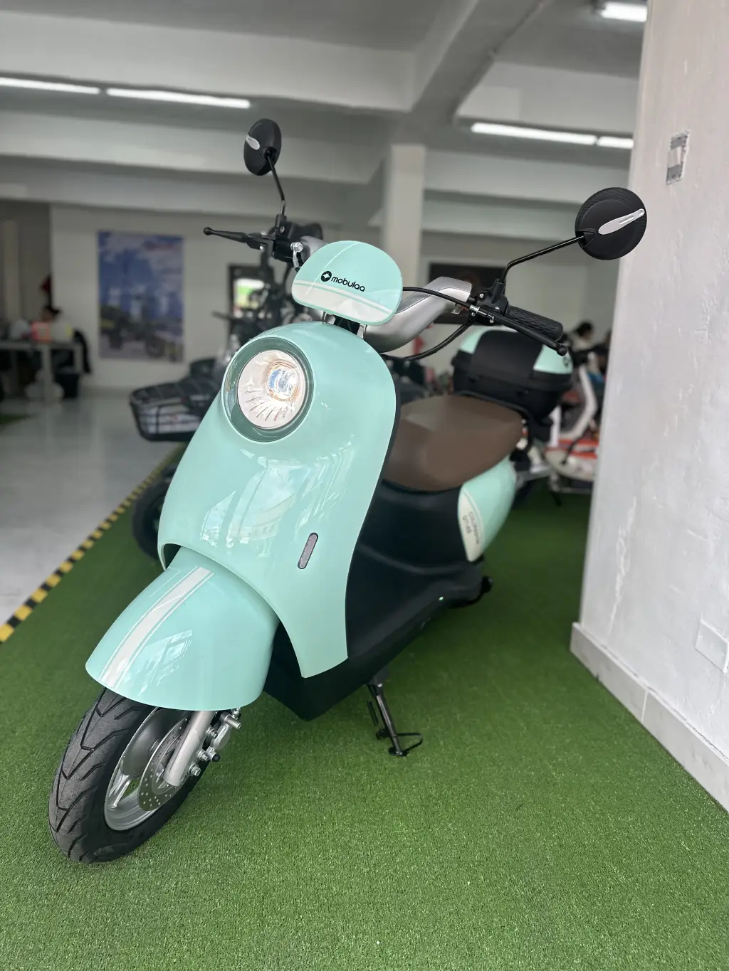 Scooter eléctrico blanco y verde con batería de litio, estacionado en un área recreativa al aire libre.