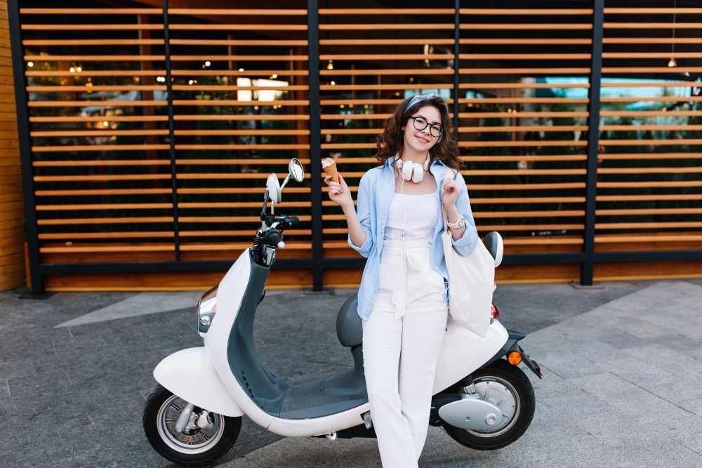Mujer joven junto a scooter eléctrico blanco en entorno urbano moderno, símbolo de movilidad sostenible