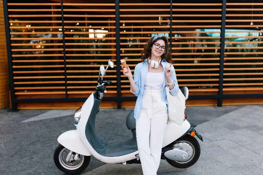 Mujer joven junto a scooter eléctrico blanco en entorno urbano moderno, símbolo de movilidad sostenible