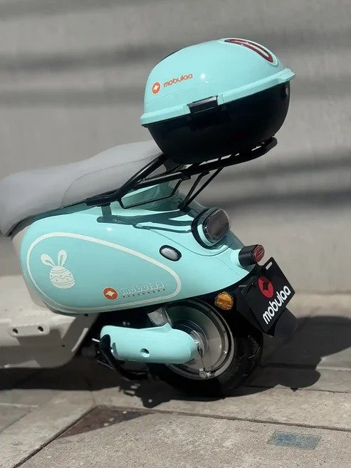 Bicicleta eléctrica Mobulaa color azul pastel con baúl trasero y diseño compacto, ideal para movilidad urbana con estilo moderno y sostenible.