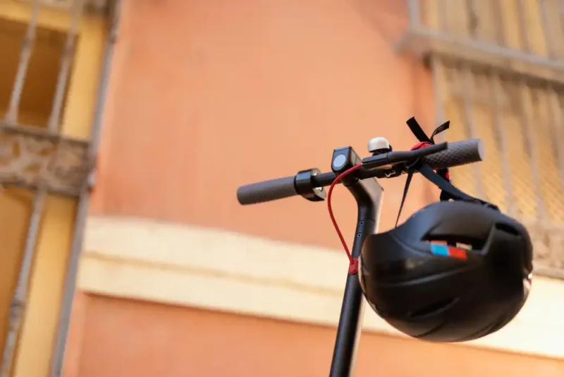 Detalle del manubrio de una patineta eléctrica con casco de seguridad colgado conforme a las normas de micromovilidad